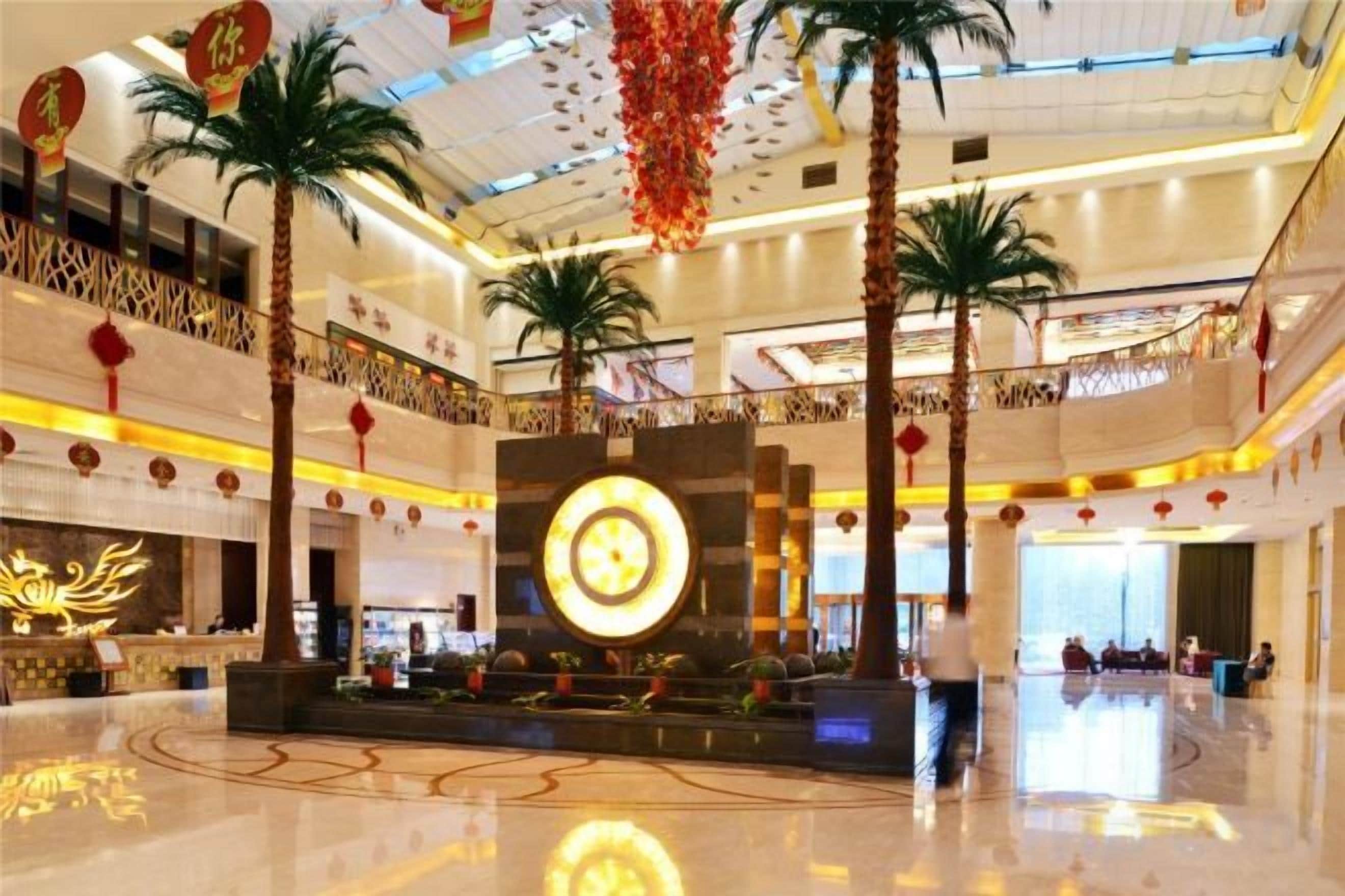 A spacious lobby with a central reception area, palm trees, and a large illuminated sign.