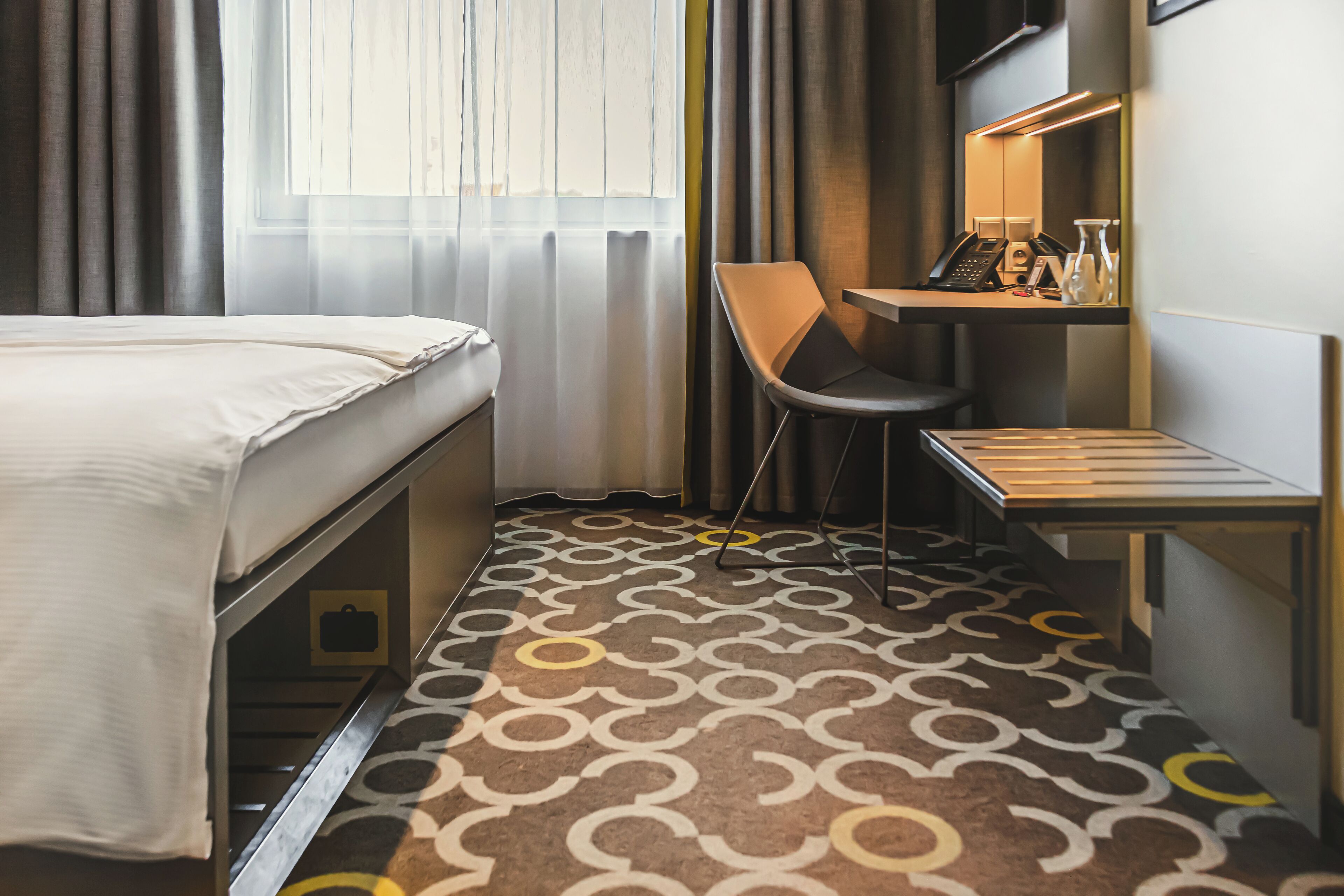 Een hotelkamer met een bed, een bureau met stoel, een telefoon en een kleine tafel.
