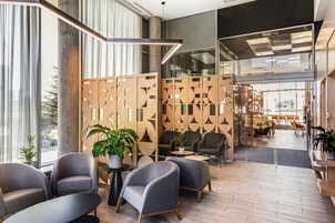 A modern lobby with grey armchairs, a wooden partition with geometric patterns, and a view of the outdoor seating area.