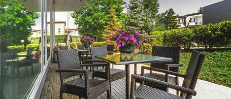 An outdoor patio with wicker furniture, a glass table, and potted plants.
