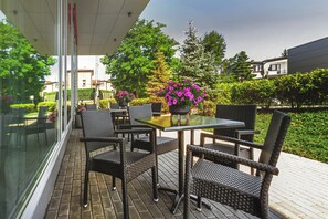 An outdoor patio with wicker furniture, a glass table, and potted plants. - Qubus Hotel Żory (Zory)