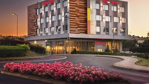 A modern hotel building with a prominent sign, multiple windows, and a landscaped entrance area with flowers. - Qubus Hotel Żory (Zory)