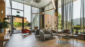 A modern lobby with wooden flooring, seating areas, and large windows offering views of the outside. - Qubus Hotel Żory (Zory)