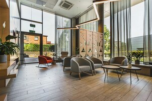 A modern lobby with wooden flooring, seating areas, and large windows offering views of the outside.