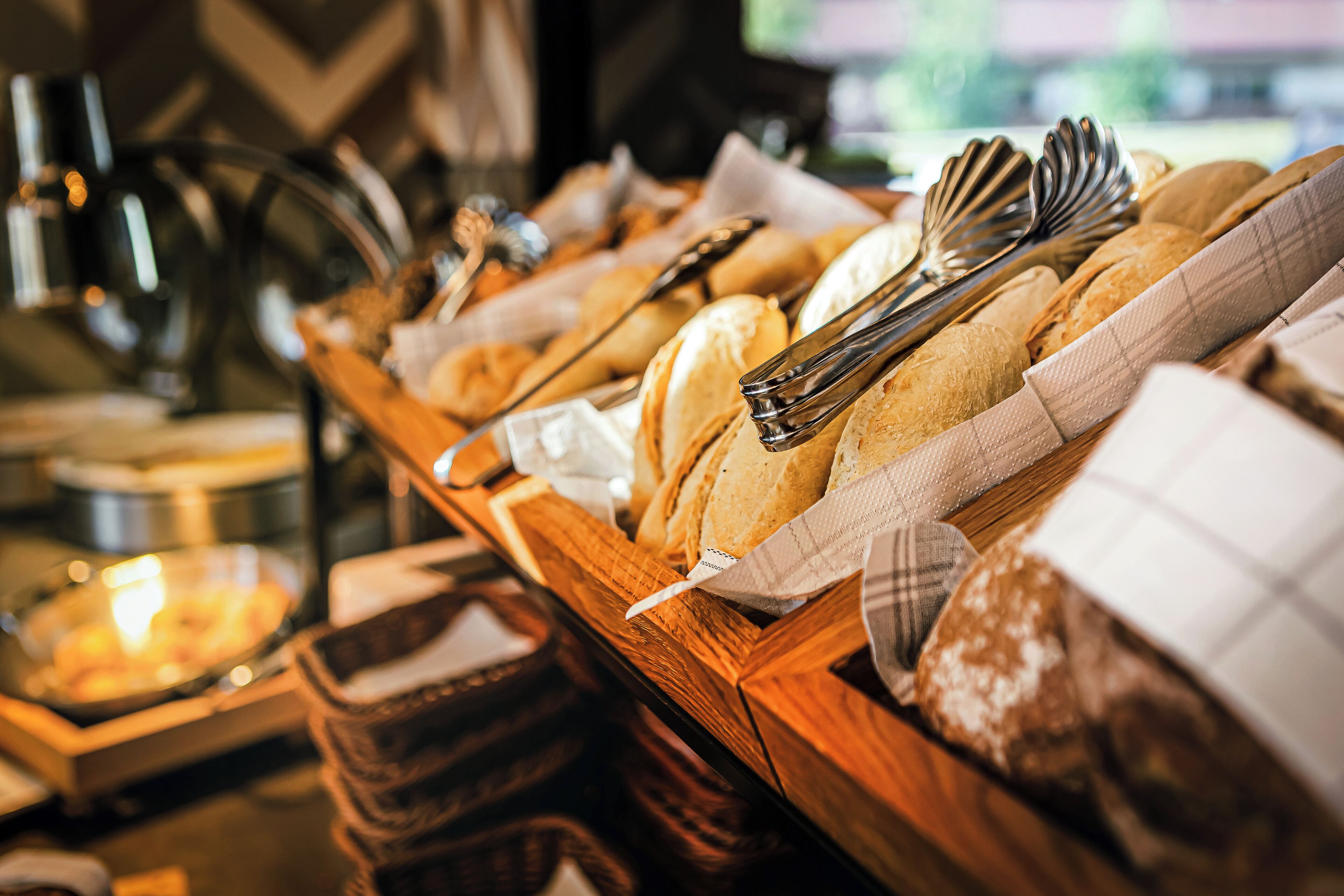 A buffet with various breads and pastries, accompanied by serving utensils.