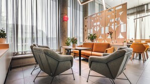 A modern hotel lobby with grey upholstered chairs, an orange sofa, and a wooden partition with geometric cutouts. - Qubus Hotel Żory (Zory)