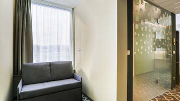 A hotel lobby with a sofa, a glass door leading to a bathroom, and patterned carpet.