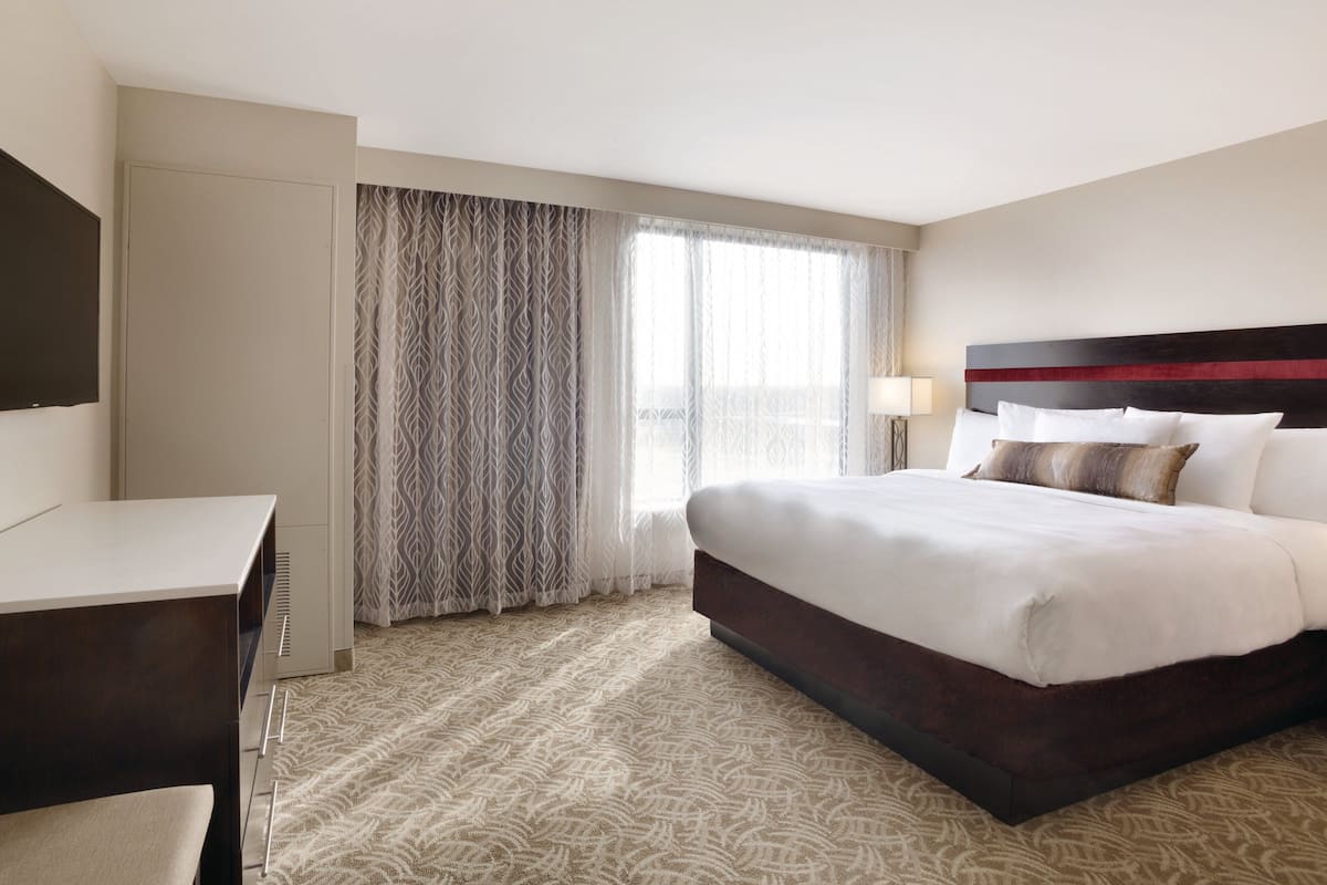 A hotel room with a large bed, a desk, and a window with curtains.