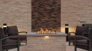 A stone fireplace with a fire, flanked by two chairs and two wall-mounted lights.
