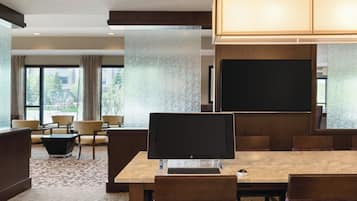 Uma sala de conferências de hotel com uma mesa grande, cadeiras, um computador e uma tela de projetor.