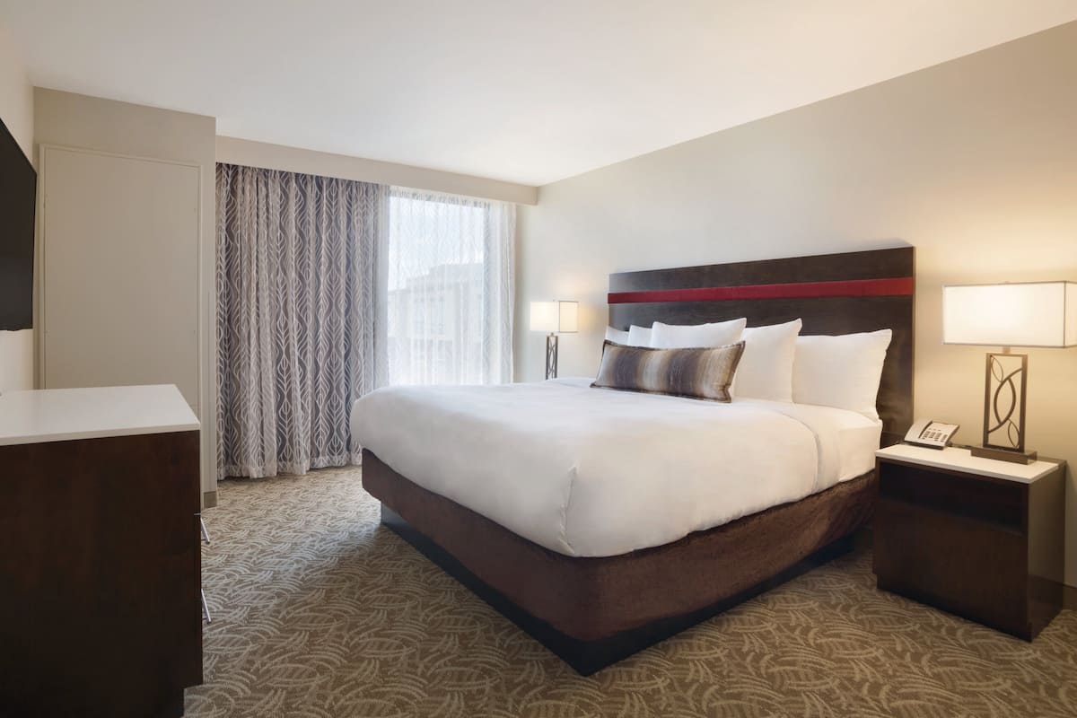 A hotel room with a large bed, a bedside table with a lamp, a wardrobe, and a window with curtains.