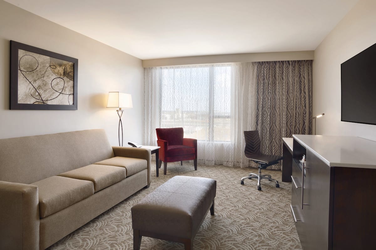 A hotel room with a sofa, a red chair, a desk, and a television.