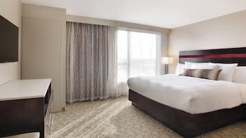 A hotel room with a bed, a desk, a lamp, and a window with curtains.