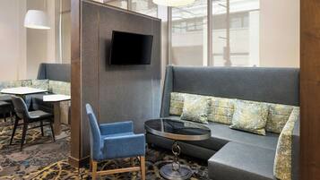 A modern hotel room with a sectional sofa, a round coffee table, and a flat-screen TV mounted on a partition wall.