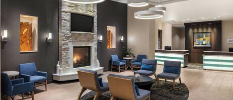 A modern lobby with a stone fireplace, blue seating, and a reception desk.