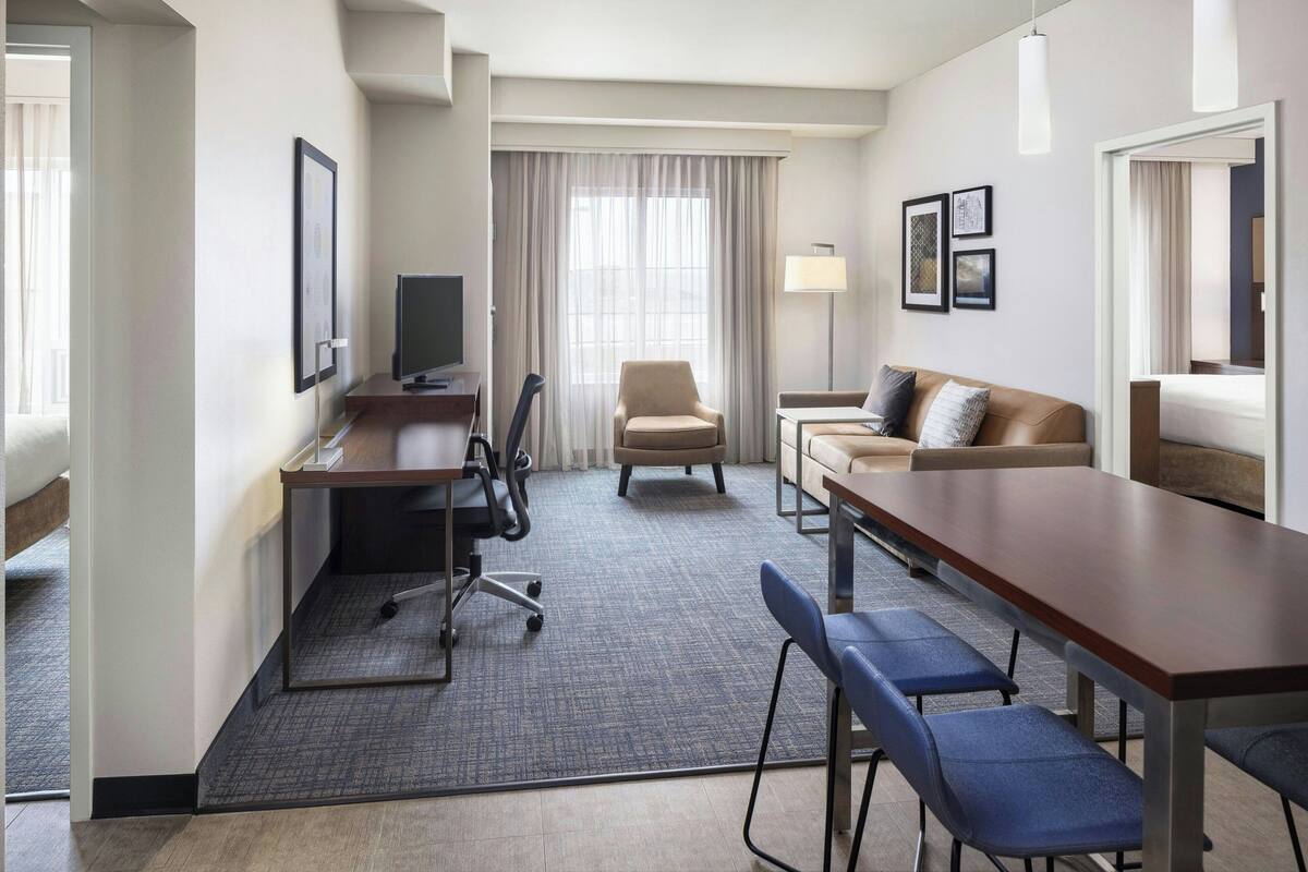 A hotel room with a desk, chair, sofa, and a large window with curtains.