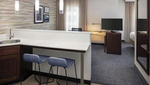 A modern hotel room with a kitchen area, a dining table, two bar stools, a flat-screen TV, and a large mirror. - Residence Inn Ann Arbor Downtown (Ann Arbor)