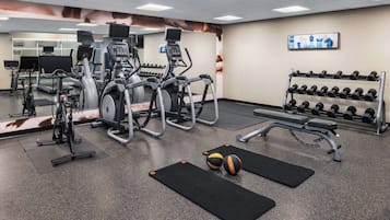 Uma academia com diversos equipamentos de exercício, incluindo esteiras, elípticos e um banco.