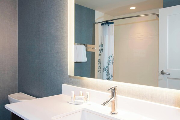 A modern bathroom with a white sink, a mirror, and a shower curtain.