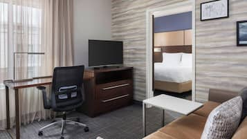 A hotel room with a bed, a desk with a chair, a TV, and a small table.