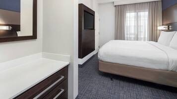 A hotel room with a bed, a TV mounted on a wall, a desk with drawers, and a window with curtains.