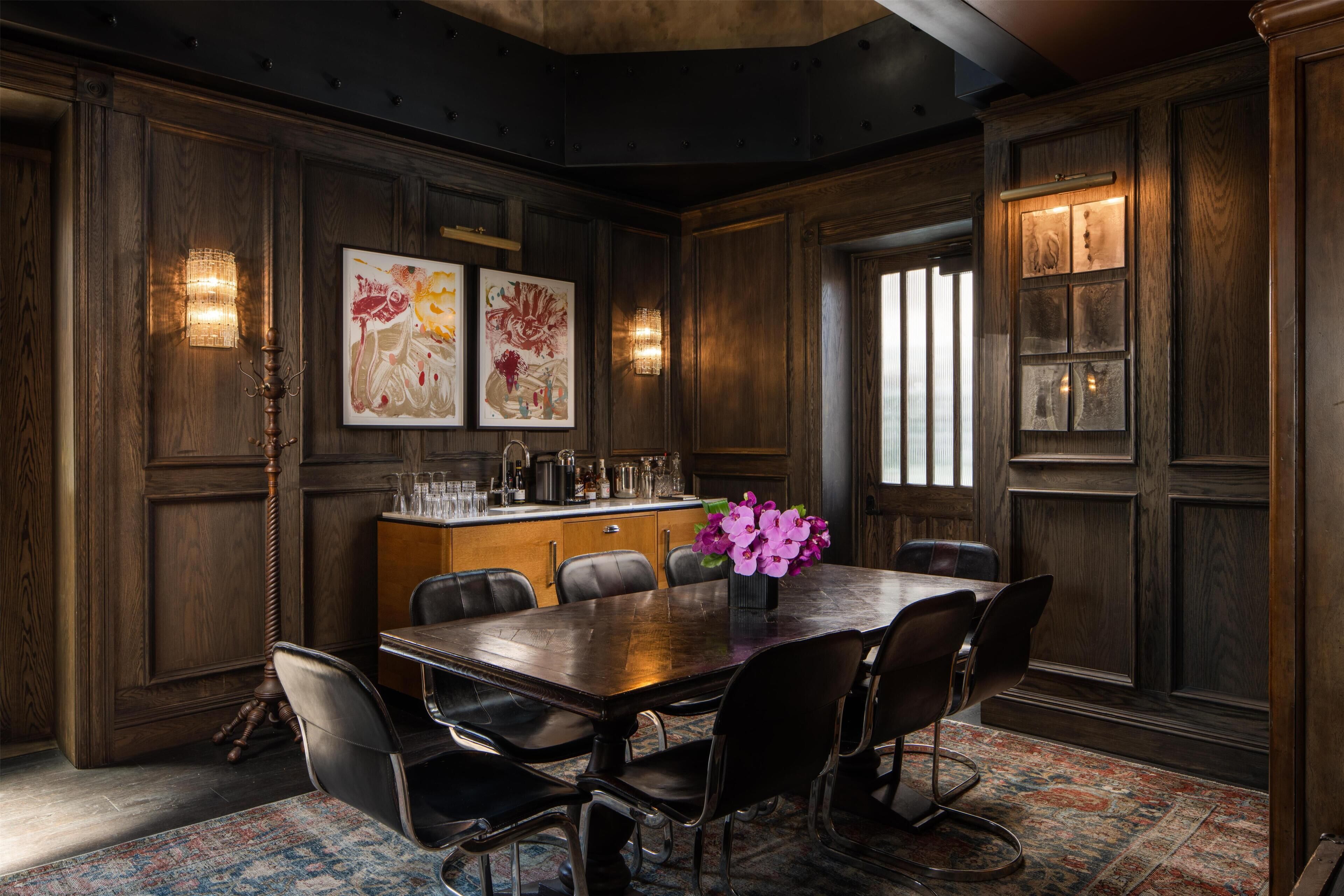 A dining area with a wooden table, chairs, artwork, and wall sconces.