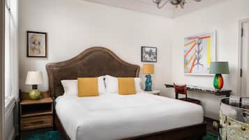 A hotel room with a large bed, a nightstand with a lamp, a chair, a desk with a lamp, and artwork on the walls.