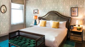 A spacious bedroom with a large bed, a wooden headboard, a green upholstered bench, a chandelier, and patterned wallpaper.
