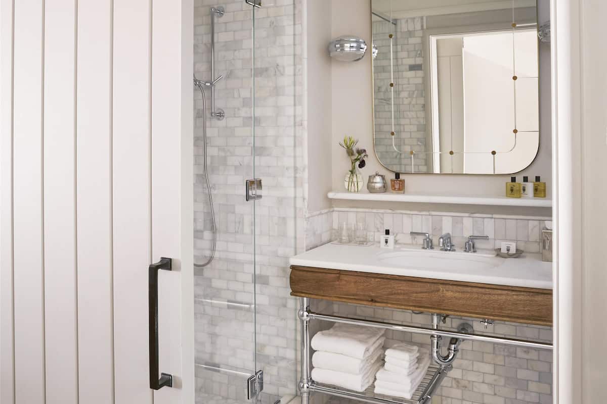 Um banheiro com box de vidro, toucador branco com bancada de madeira e piso revestido de azulejos.