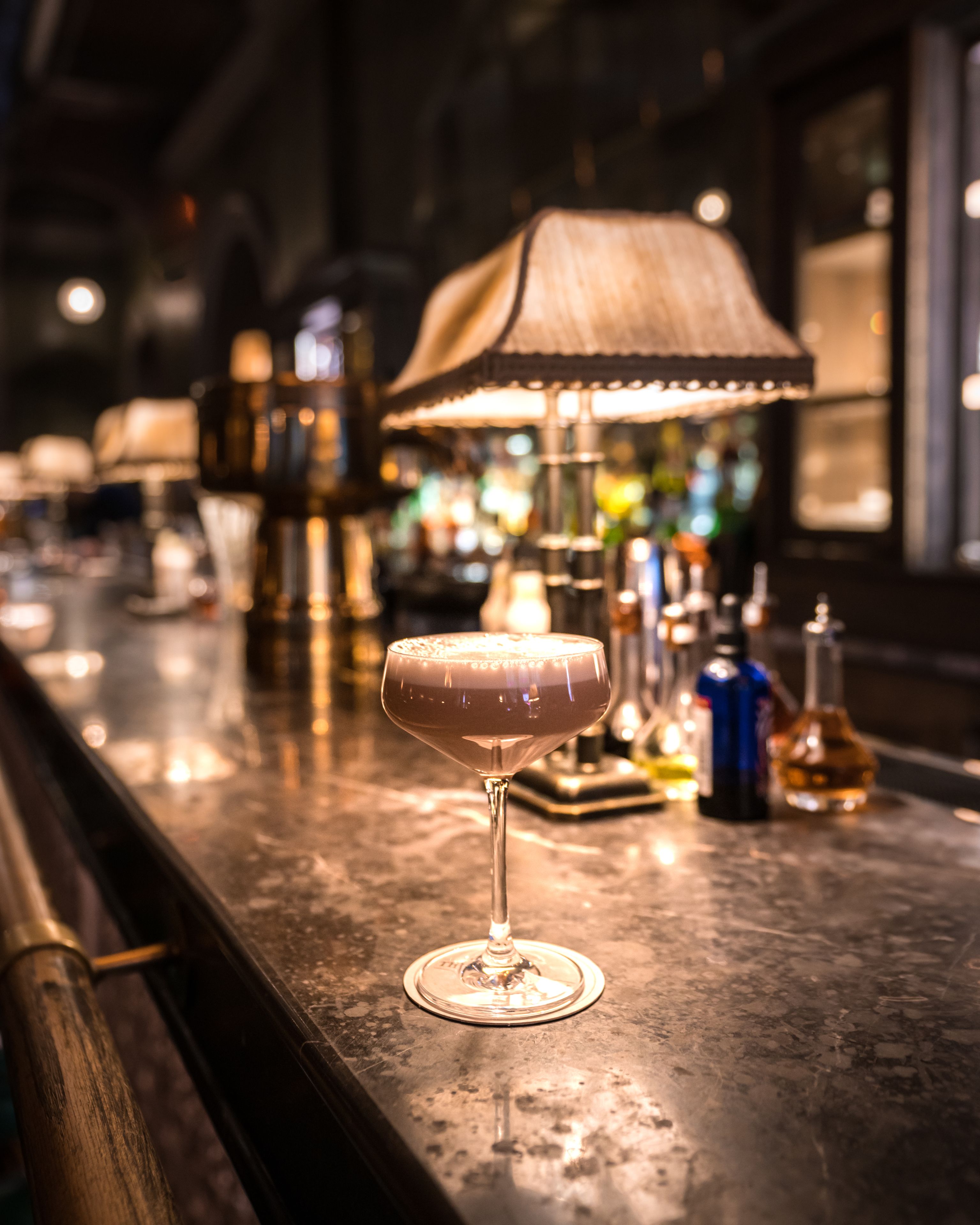 A bar area with a cocktail glass on the counter, a lamp, and various bottles.