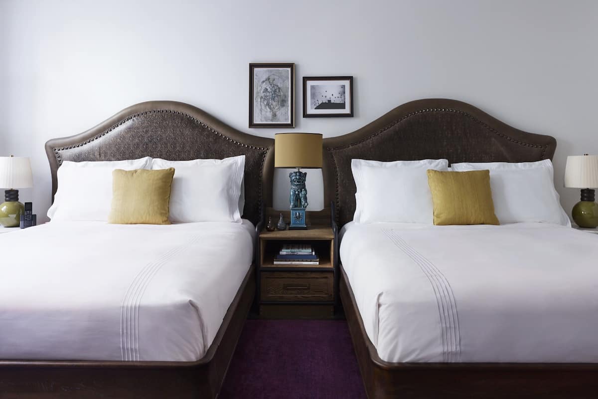 Quarto de casal com duas mesas de cabeceira, cada uma com luminária e uma mesinha.