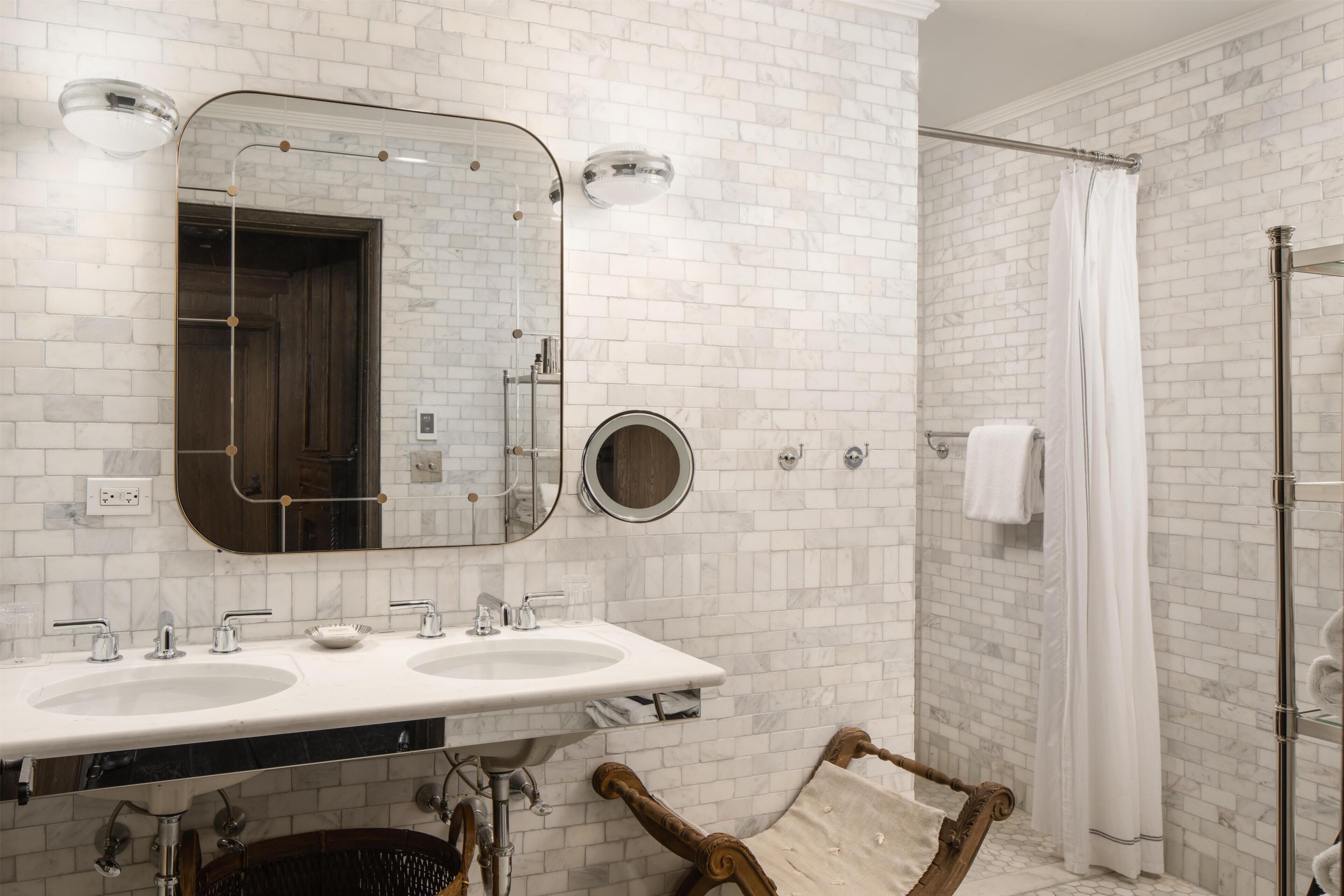 A bathroom with white brick walls, two sinks, a large mirror, and a shower area.