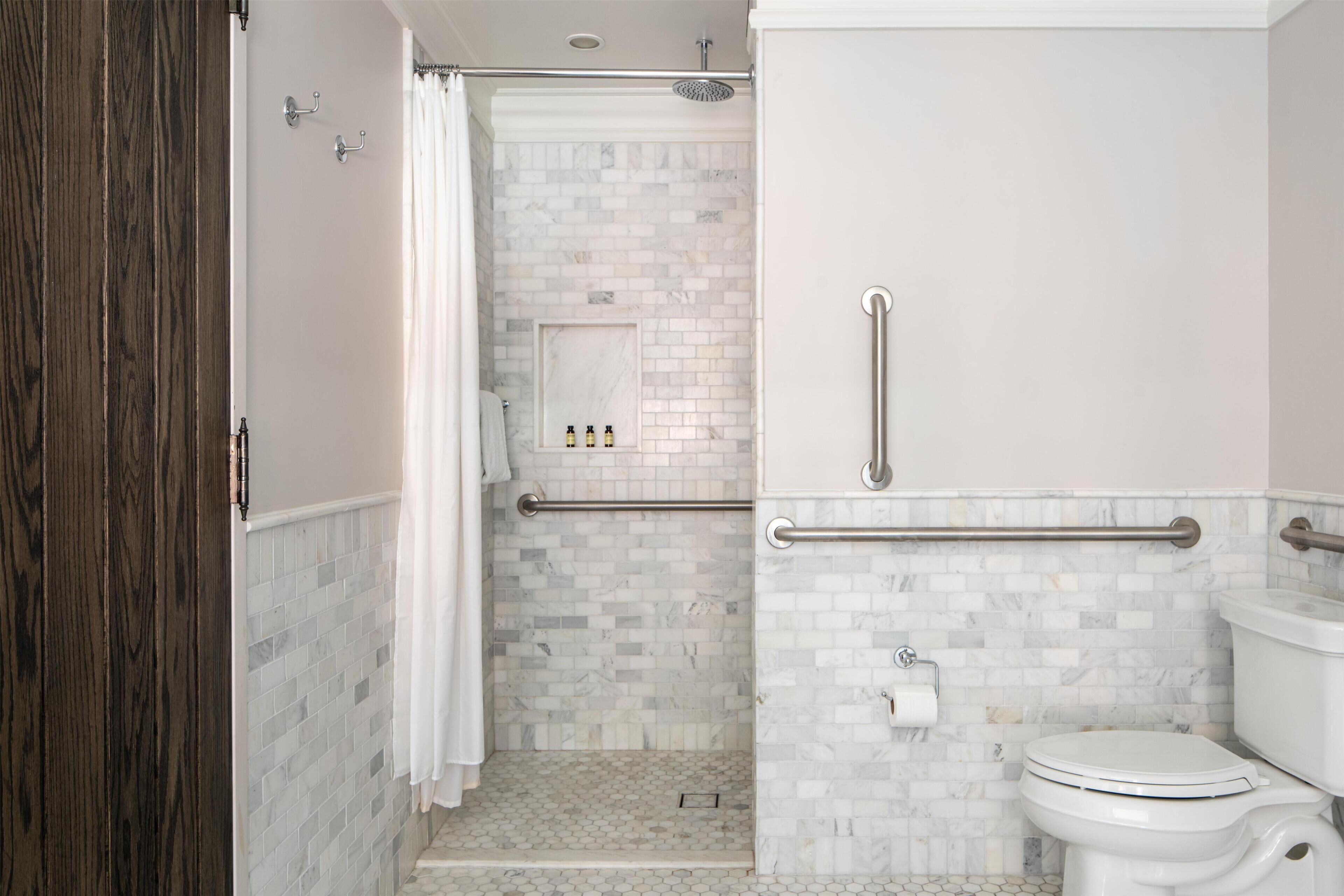 A bathroom with a shower, toilet, and grab bars.