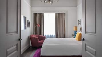 Une chambre d’hôtel avec un grand lit, un fauteuil rouge, un lustre et une vue sur l’extérieur par la fenêtre.