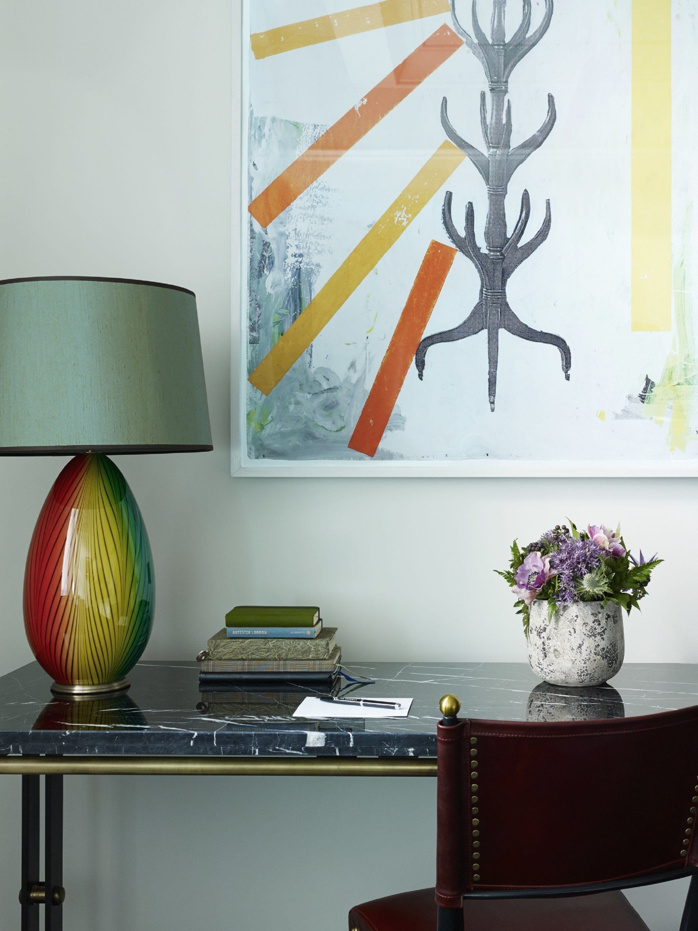 Un bureau agrémenté d’une lampe colorée, d’une plante en pot et d’une œuvre d’art encadrée.