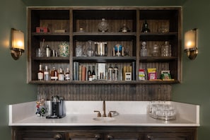 A kitchen with a wooden shelf unit above a white countertop, containing various kitchen items and bottles.