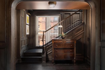 A restaurant interior with round tables, bar stools, hanging light fixtures, and a clock on the wall. at The Beekman, A Thompson Hotel, by Hyatt