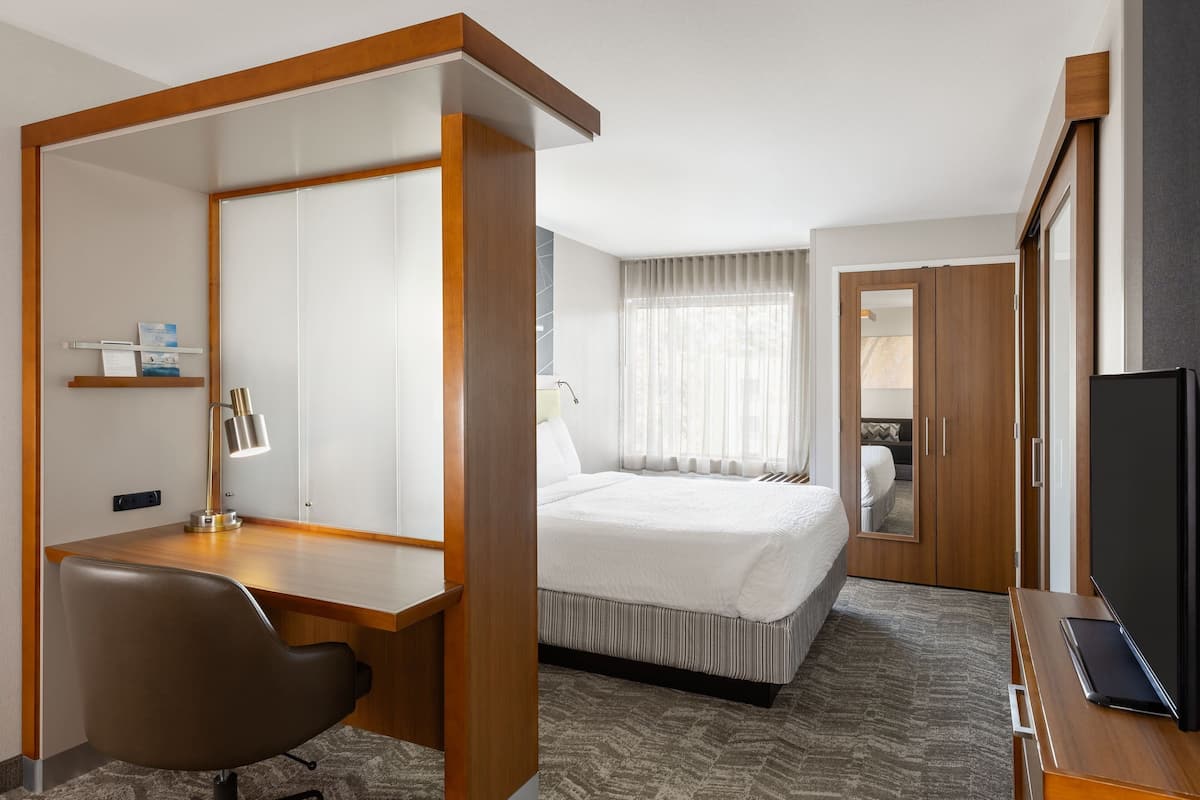 A hotel room with a bed, a desk, a chair, a TV, and a wardrobe.