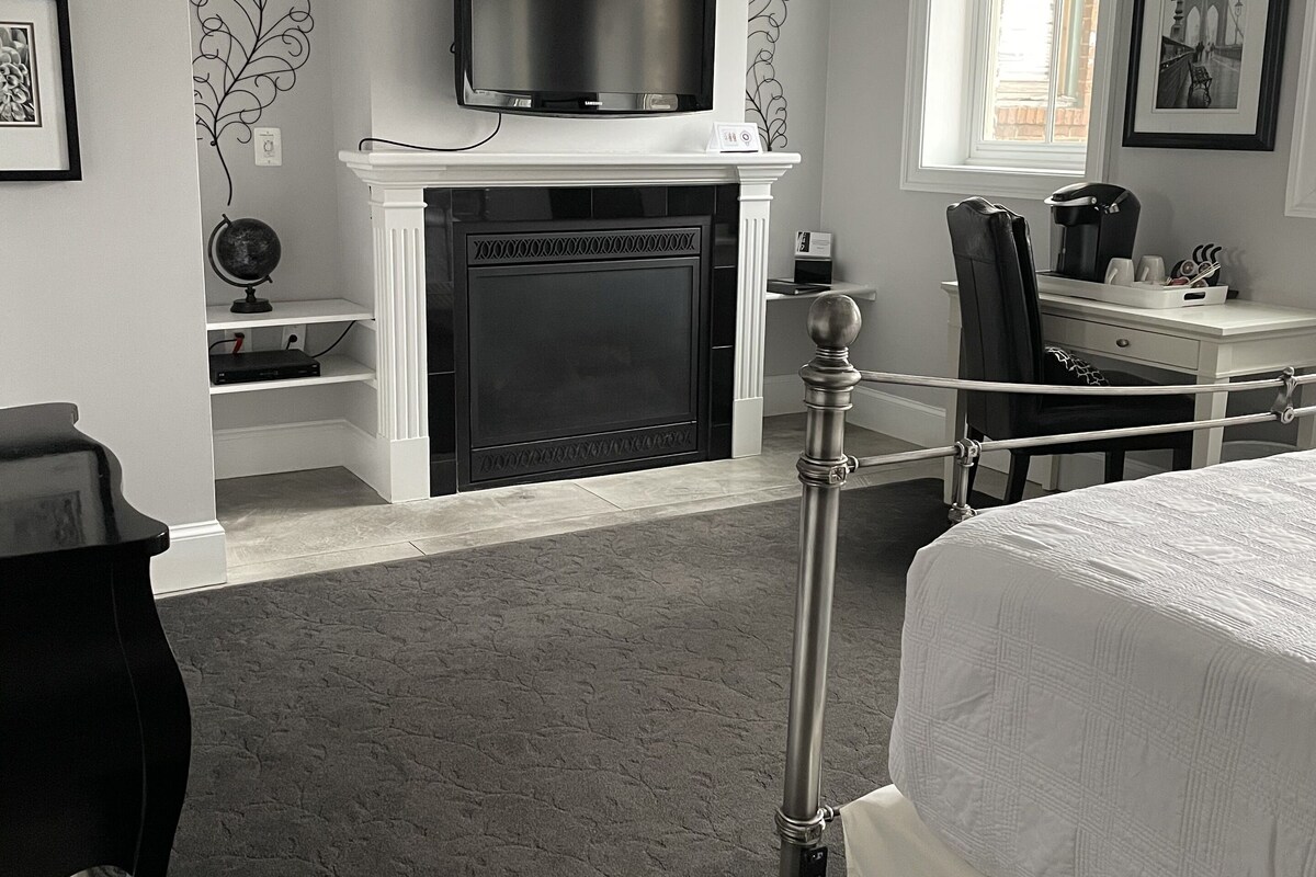 A bedroom with a fireplace, a bed, a desk, and a television.