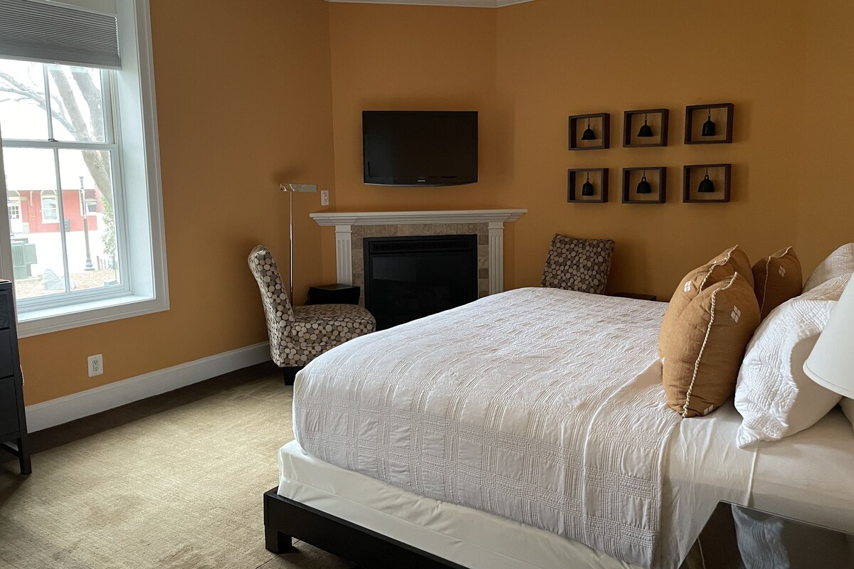 A bedroom with a large bed, a fireplace, a chair, and a TV mounted on the wall.