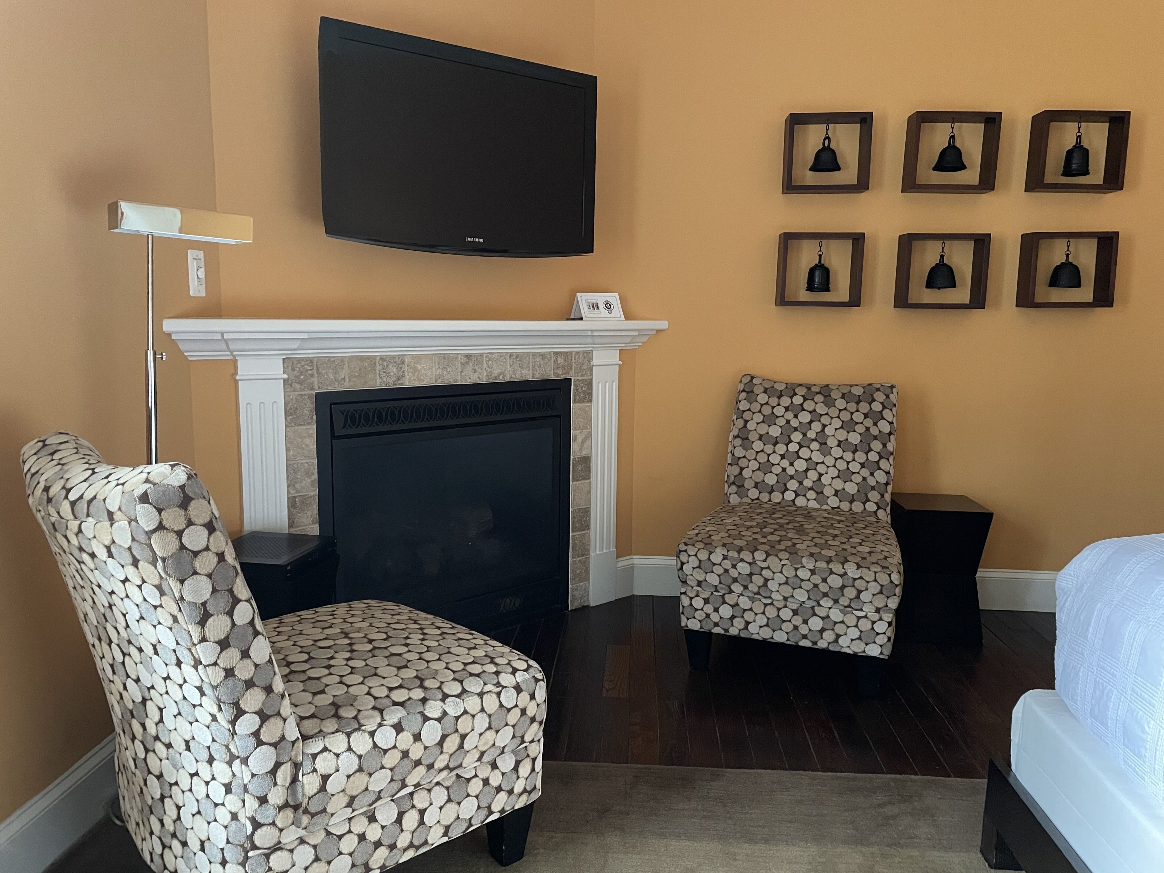 A living room with a fireplace, two patterned armchairs, a flat-screen TV, and framed wall decorations.