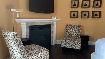A living room with a fireplace, two patterned armchairs, a flat-screen TV, and framed wall decorations.
