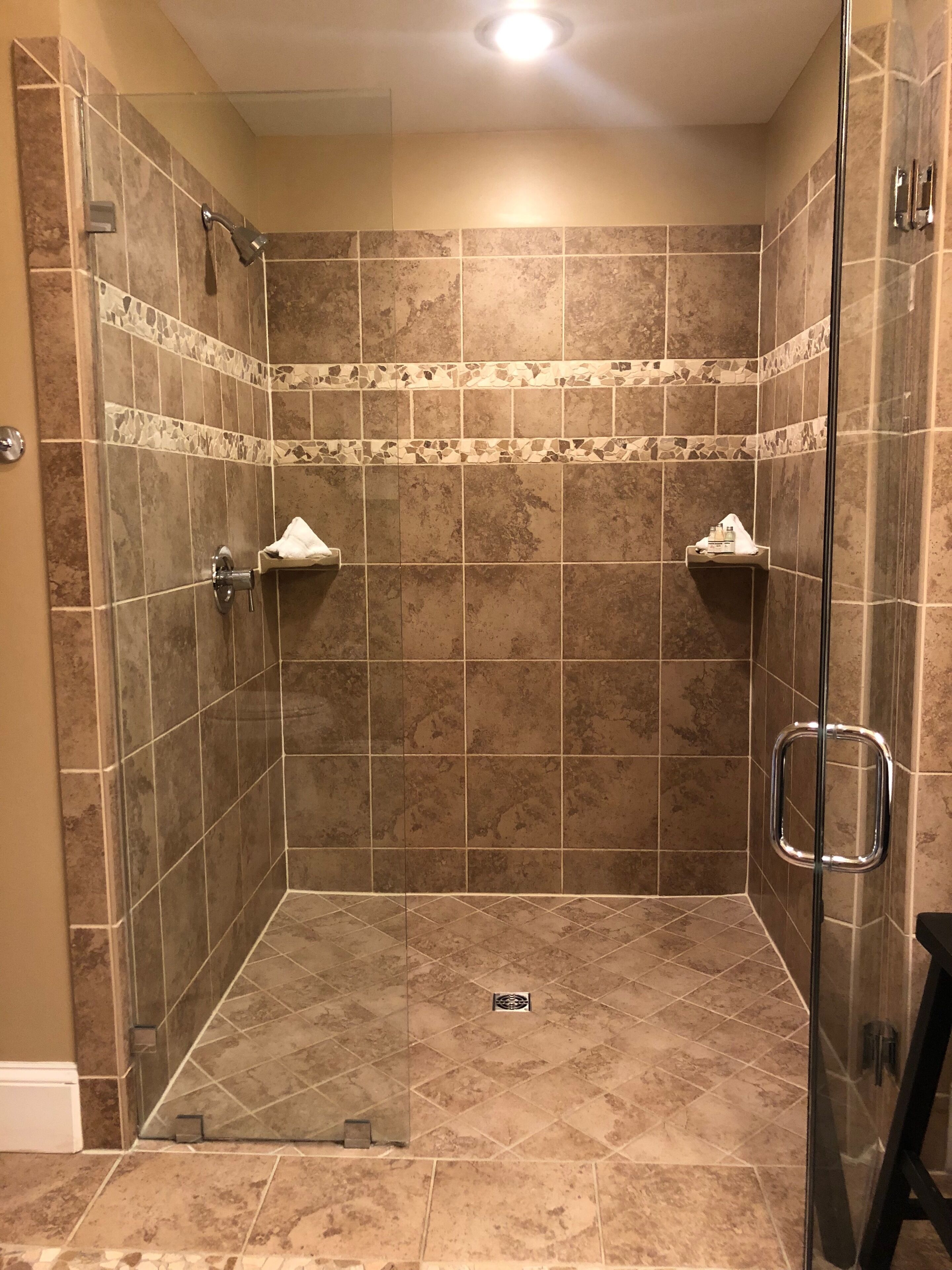 Une douche à l’italienne avec une porte en verre, des murs carrelés et une petite étagère pour les articles de toilette.