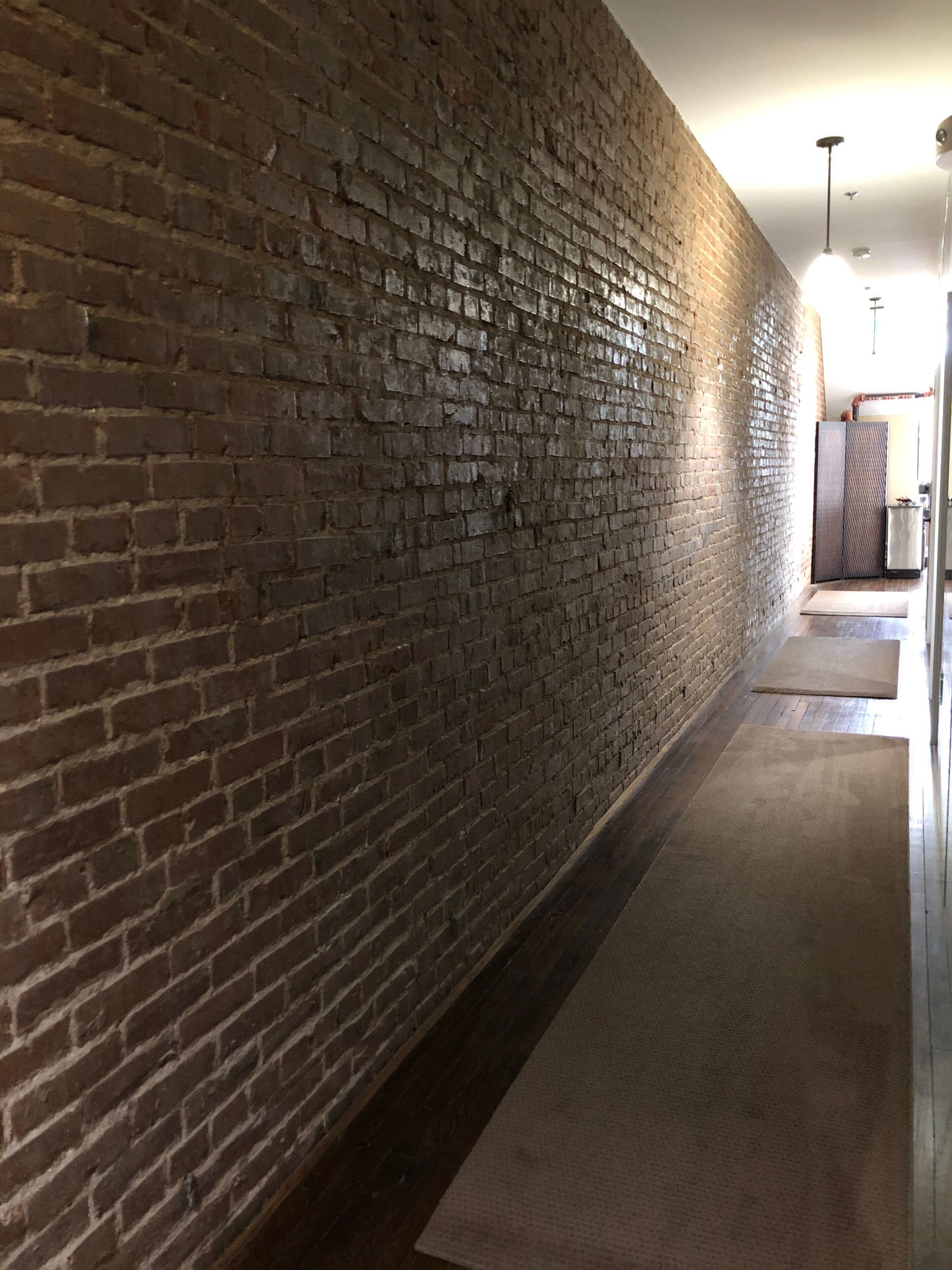Un pasillo con pared de ladrillo, suelo de madera y una lámpara colgante.