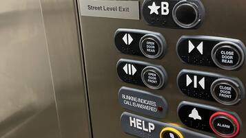 Panel de control de ascensor con botones para 'Suites & Fitness Room', 'Salón de Banquetes' y 'Salida a Nivel de Calle'.