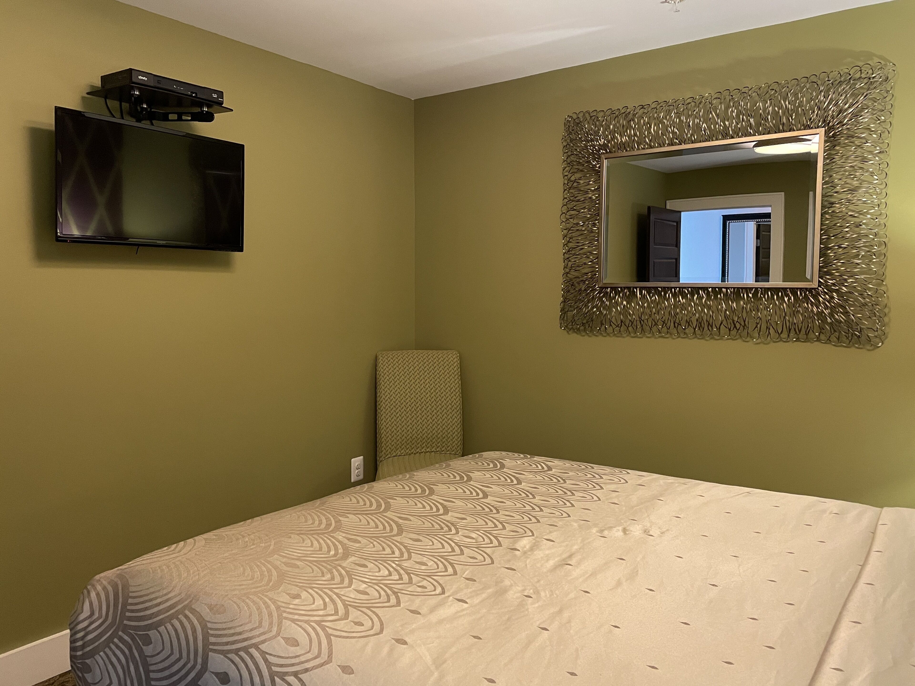 A bedroom with a bed, a television mounted on the wall, and a decorative mirror.