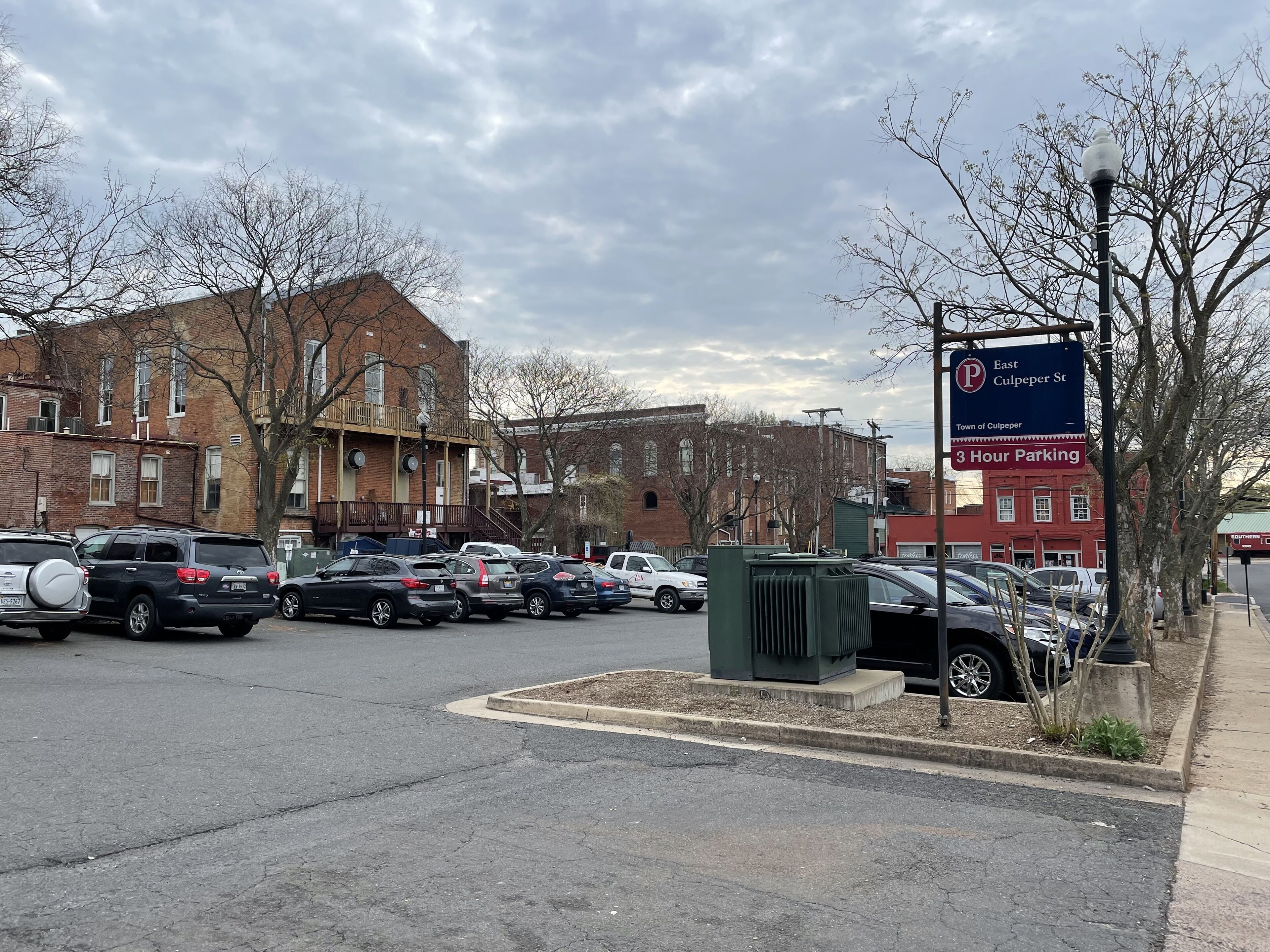 A parking lot with multiple cars, a sign indicating East Culpeper St, and brick buildings in the background.