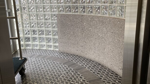Esquina de una habitación con piso a cuadros, baranda de metal y pared con textura.