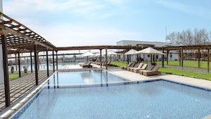 A swimming pool with lounge chairs and umbrellas, surrounded by a pergola and a view of a building in the background.