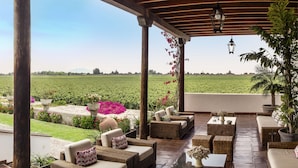 An outdoor patio with wicker furniture, a view of a green field, and a pergola structure.